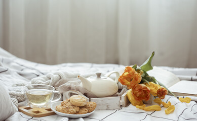 Spring home composition in bed with a cup of tea, cookies, a teapot, a book and a bouquet of flowers copy space.