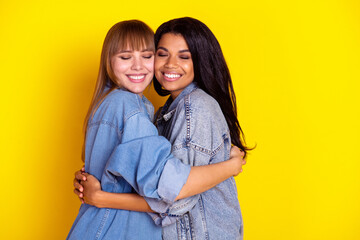 Profile photo of two pretty positive girls diversity closed eyes toothy smile hugging isolated on yellow color background