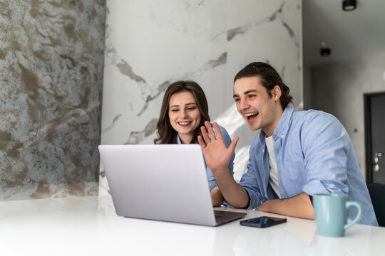 Happy young couple smiling looking at laptop screen making video call in the kitchen.