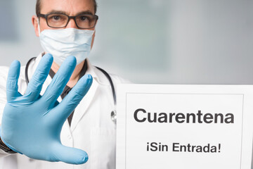 Doctor with medical face mask and medical gloves showing a spanish quarantine sign in front of a...