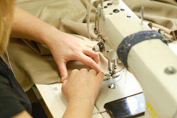 Female hands stitching white fabric on professional manufacturing machine at workplace. Close up view of sewing process. Light blurred background
