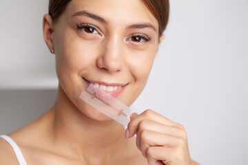 Teeth whitening, beautiful smiling woman holding a whitening strip.