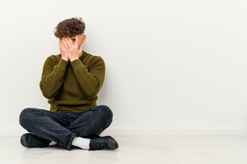 Young Moroccan man sitting on the floor isolated on white background blink through fingers frightened and nervous.