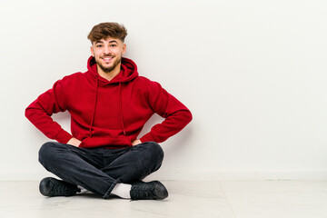 Young Moroccan man sitting on the floor isolated on white background confident keeping hands on hips.