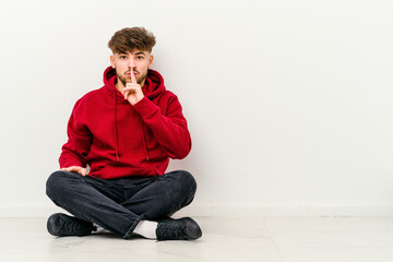 Young Moroccan man sitting on the floor isolated on white background keeping a secret or asking for silence.