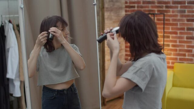 Positive emotional woman shaves a lock of hair with a clipper at the mirror. The woman is happy to change her style with a new hairstyle.