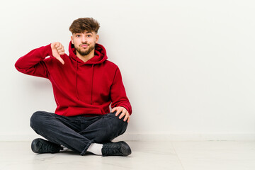 Young Moroccan man sitting on the floor isolated on white background showing thumb down, disappointment concept.