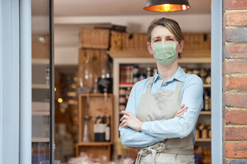 Portrait Of Female Owner Standing Outside Delicatessen Wearing Face Mask During Health Pandemic