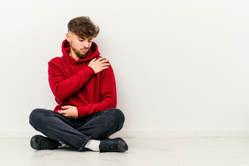 Young Moroccan man sitting on the floor isolated on white background having a shoulder pain.