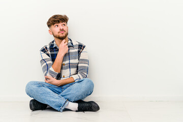 Young Moroccan man sitting on the floor isolated on white background thinking and looking up, being reflective, contemplating, having a fantasy.