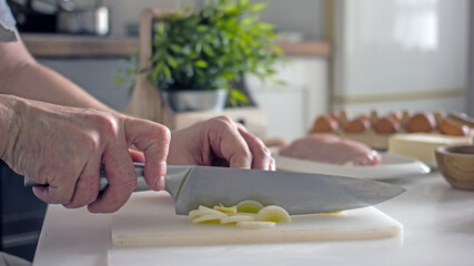 Slicing green leeks with a knife close-up, authentic photo of food preparation. Male hands with a knife cut a leek