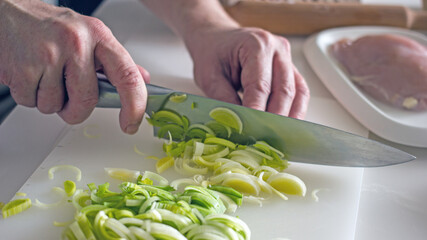 Slicing green leeks with a knife close-up, authentic photo of food preparation. Male hands with a knife cut a leek