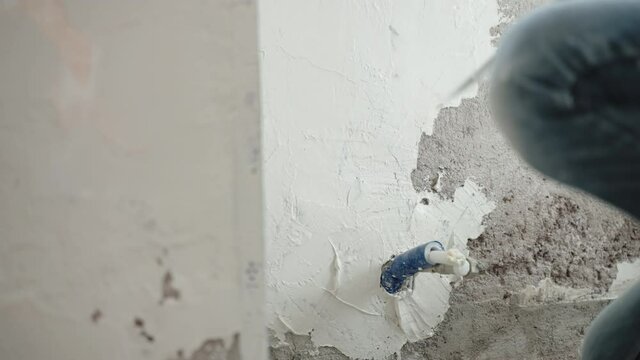 Builder plastering cement wall using metal trowel, spatula and white spackling paste, man leveling and aligning wall surface with putty stucco. Walls renovation, repairing works concept