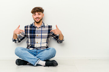 Young Moroccan man sitting on the floor isolated on white background points down with fingers, positive feeling.