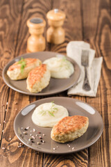 Chicken cutlets on gray plates with white garlic sauce on a wooden background with a fork for eating.