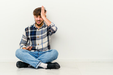 Young Moroccan man sitting on the floor isolated on white background forgetting something, slapping forehead with palm and closing eyes.