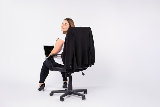 A photo from the back of a large size business woman in a black chair with notebooks in her hands looks into the camera with a smile. White background with side space.