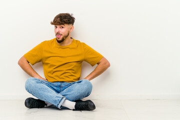 Young Moroccan man sitting on the floor isolated on white background funny and friendly sticking out tongue.