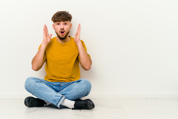 Young Moroccan man sitting on the floor isolated on white background surprised and shocked.