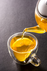 Pouring ginger tea with lemon and honey in crystal glass on black background