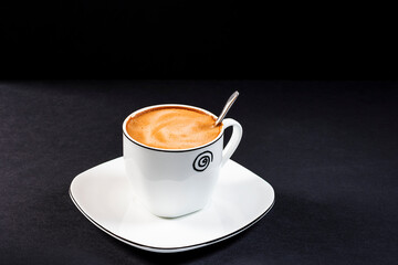 Creamy latte in a porcelain cup with saucer.Horizontal format photography taken in studio with artificial light.