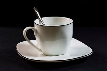 Porcelain cup, spoon and plate on black background.Photography is a horizontal shot taken in a studio with artificial light.