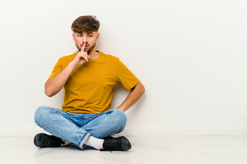 Young Moroccan man sitting on the floor isolated on white background keeping a secret or asking for silence.