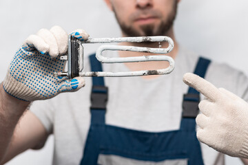 A worker points a finger at a broken, corrosive heating element. Close-up