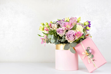 Beautiful bouquet of flowers in round box and pink gift box on a white table. Gift for holiday,...