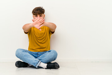 Young Moroccan man sitting on the floor isolated on white background doing a denial gesture