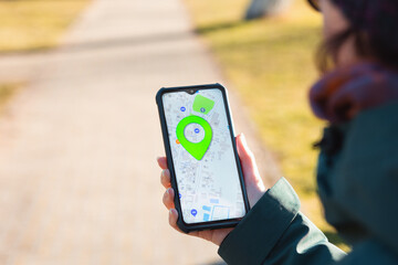 A woman holds a cellphone with the online maps app open and looks at the marked location. Close up of hand. The concept of online navigators and modern technologies