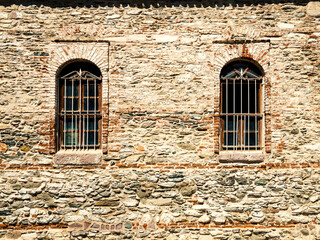 Fototapeta na wymiar Two windows with rusty metal grids on a stone wall. Architectural texture. Historical prison facade with brick surface. Medieval construction
