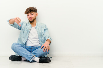 Young Moroccan man sitting on the floor isolated on white background showing thumb down, disappointment concept.