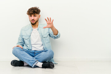 Young Moroccan man sitting on the floor isolated on white background showing claws imitating a cat, aggressive gesture.