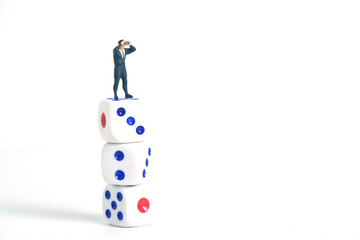 Miniature people toys photography. A businessman looking, searching, observing using binoculars above the dice isolated on white background.