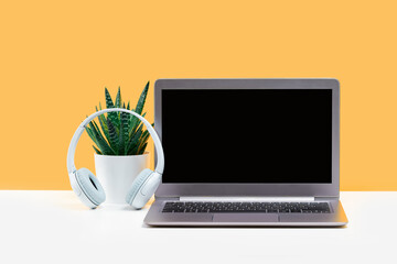 Fototapeta premium Laptop. Mockup screen and headphones on white desk and plain yellow background banner. Distant learning. working from home, online courses or support minimal concept. call center headset