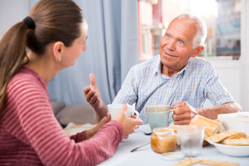 Senior man talking with young sad daughter at table with food and pointing to mistakes
