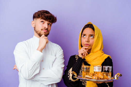 Young Moroccan couple drinking tea celebrating ramadan month isolated on purple background
