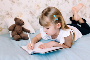 Fototapeta na wymiar Girl writes in blue book on bad. Education concept. Home schooling. Homework.