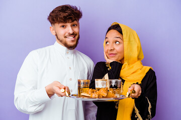 Young Moroccan couple drinking tea celebrating ramadan month isolated on purple background