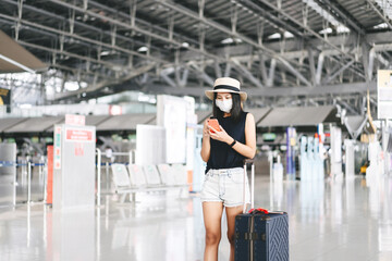 Fototapeta na wymiar Adult tourist woman with luggage wear mask for covid-19 check in with mobile phone at airport terminal.