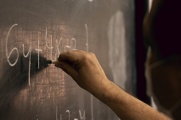Teacher wearing mask writing equations on a blackboard. Covid situation, pandemic, new normal....