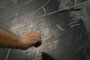 Hand writing maths equations with chalk on a blackboard. Perspective from below.