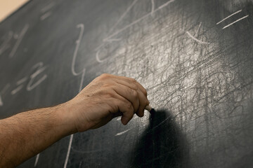 Hand writing maths equations with chalk on a blackboard. Perspective from below.