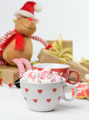 white ceramic cup with cocoa and marshmallows, behind a gift box and a Christmas toy