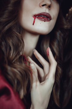 Vampire woman with bloody lips. Vampire lips in blood. Vampire Teeth. Bloody mouth of a vampire with fangs and bloodstained hand.  Vampire with open mouth and fangs. 