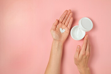 Revitalizing hand cream for healing and recovery after excessive use of soap and disinfectants. Young woman applying moisturizing lotion. Copy space, close up, pink background, flat lay, top view.