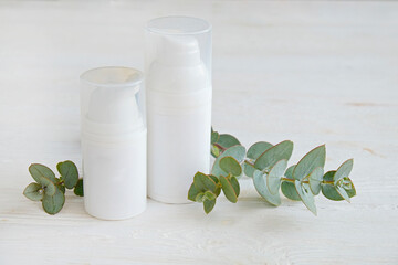 Obraz na płótnie Canvas Two plastic bottles of different size with the dispenser cap and blank label with copy space for text or logo, white wood textured table background. Eucalyptus leaves as decor. Close up, top view.