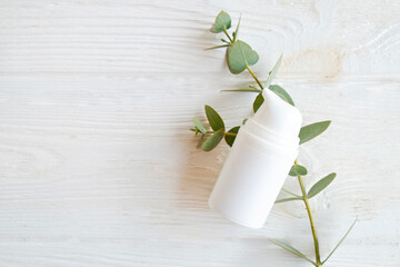 Single plastic bottle with the dispenser cap and blank label with copy space for text or logo, white wood textured table background. Eucalyptus leaves as decor. Close up, copy space, top view.