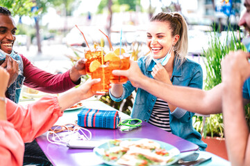 Young people drinking spritz at cocktail bar wearing face masks - New normal friendship concept...